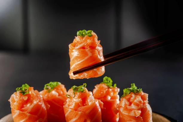 Japanese food (brazilian style) Salmon Jhow sushi on chopsticks in a black background. Closeup. sushi stock pictures, royalty-free photos & images