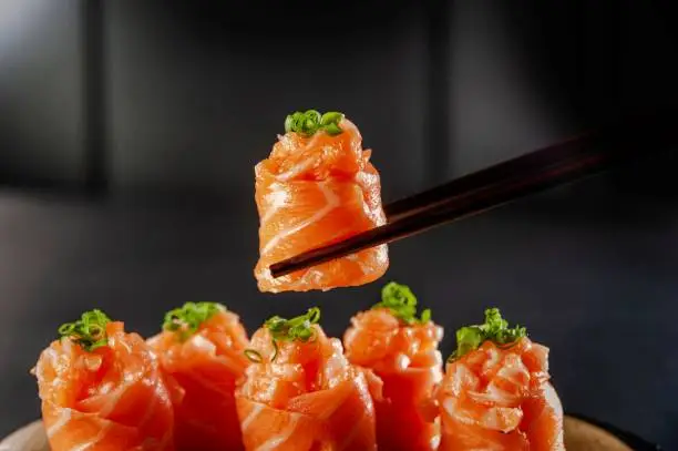 Salmon Jhow sushi on chopsticks in a black background. Closeup.
