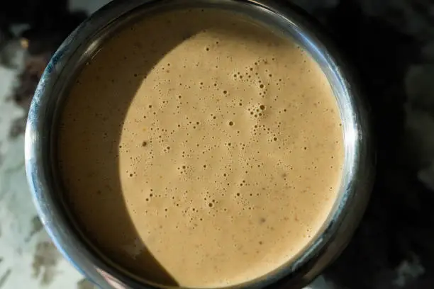 Detailed overhead view of Thai peanut sauce in a small metal bowl with shadow encroaching.