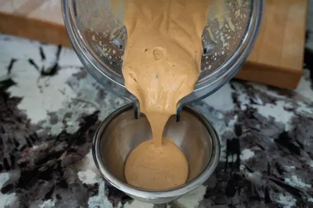 Thai peanut sauce being poured into small bowl from blender after being mixed.