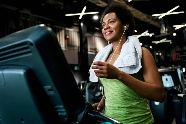 Photo of Smiling African American woman running on a treadmill in gym with towel around neck