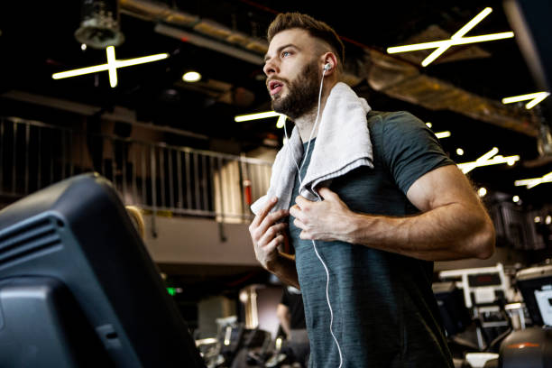 istock Young man running on a treadmill with towel around neck 1368818686