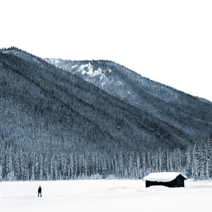 man walking with log cabin in winter mountain wilderness, square frame