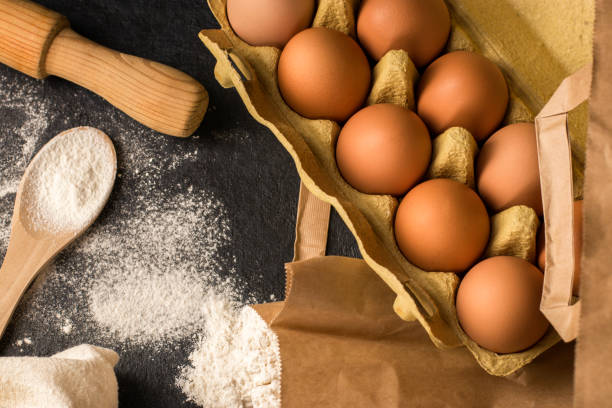 Natural fresh chicken eggs in eco package, flour, rolling pin on a dark kitchen table, linen towel. Traditional ingredients for baking. Top view. Flat lay. Kinfolk style.