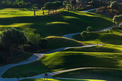 Golf course, with small mounds and paths shaded by the evening light.