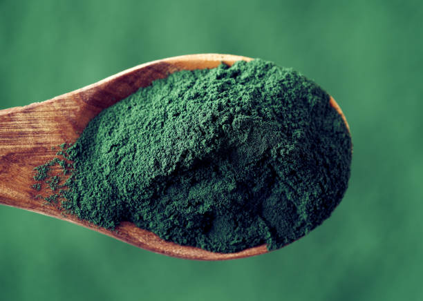 Spirulina powder on a spoon, closeup Spirulina algae powder on a wooden spoon over green background spirulina bacterium stock pictures, royalty-free photos & images