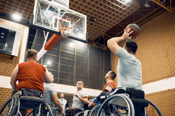 Below view of disabled men playing wheelchair basketball match on the court. Low angle view of handicapped player shooting at the hoop during wheelchair basketball sports match. sports league stock pictures, royalty-free photos & images