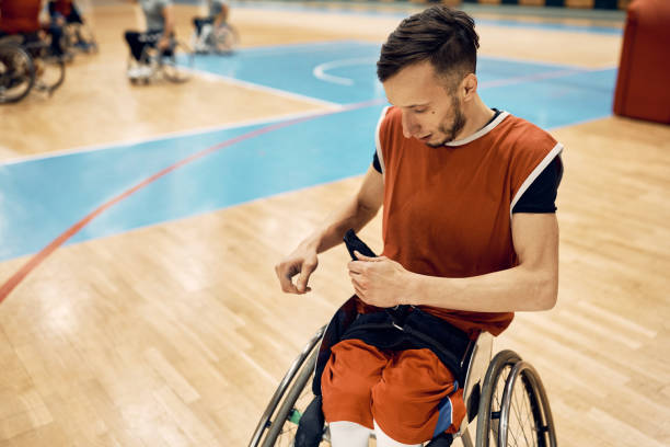 sportowiec na wózku inwalidzkim zapina pas bezpieczeństwa podczas przygotowań do meczu koszykówki na boisku. - wheelchair physical impairment disabled spinal zdjęcia i obrazy z banku zdjęć