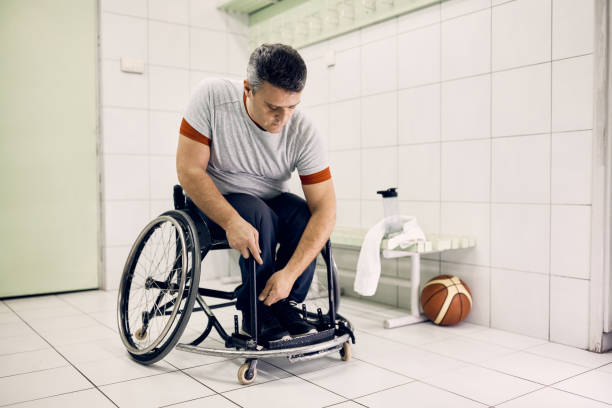 koszykarz niepełnosprawny przypinający nogi na wózku inwalidzkim w szatni - wheelchair physical impairment disabled spinal zdjęcia i obrazy z banku zdjęć