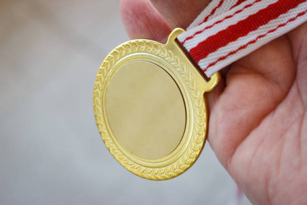 el hombre de cerca sostiene una medalla de oro en blanco en su mano. - medallista fotografías e imágenes de stock