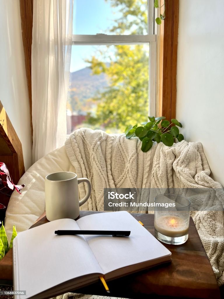 Cozy nook at home to take a break A cozy reading nook with a chair next to a window and a journal to write on. Conveys the ideas of self care and wellness. Candle Stock Photo