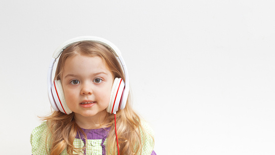 Cheerful little girl 3 years old in headphones on white background with copy space. Music or entertainment online.