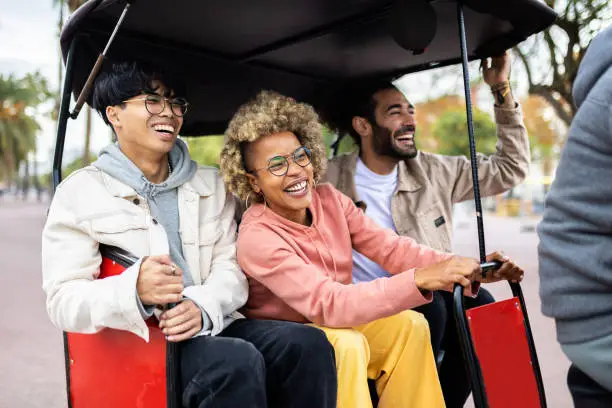Three joyful diverse tourist friends riding in tuk tuk taxi on vacation in Barcelona - Multiracial friends laughing and having fun visiting an european city on holidays