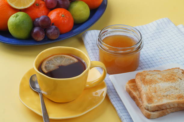 istock Breakfast - toast bread, tea with lemon, honey in a jar, fruit on a plate. And a beautiful yellow tablecloth. 1368841931