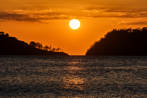 A beautiful image of the setting sun and hazy orange sky between two landmasses off the coast of Costa Rica.