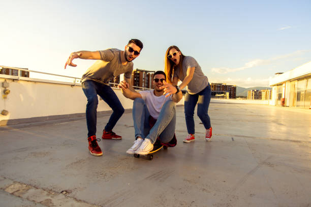istock Young cheerful friends playing and driving skateboard on the rooftop 1368853347