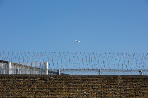 Prison wall with razor wire and an aeroplane in the background