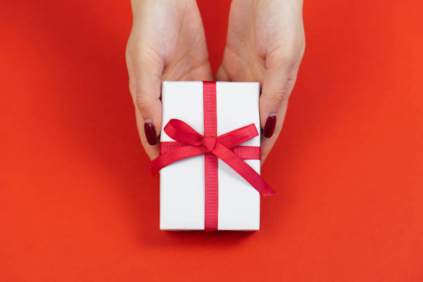 istock Woman hands hold white gift box with red bow on red table. Valentines day or bithday present concept 1368860245