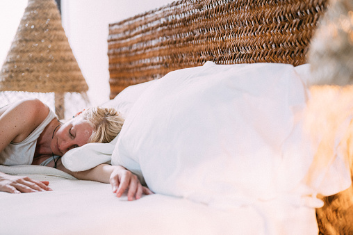 A woman sleeps on white pillows under a warm blanket in a comfortable modern boho bedroom