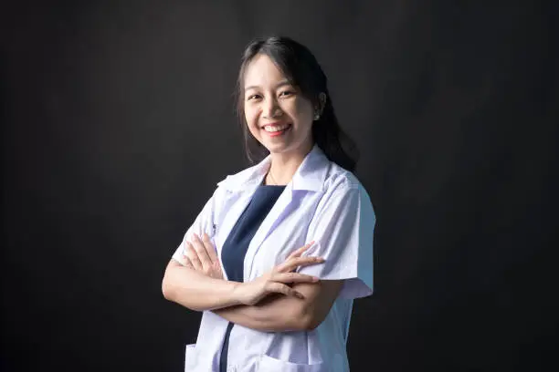 Young Asian female physician, Med student or resident doctors smile and standing on black background.