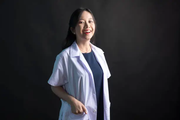 Young Asian female physician, Med student or resident doctors smile and standing on black background.