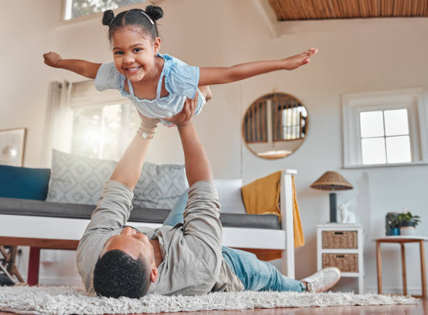 portrait of a young father and daughter bonding while playing on the floor at home - arms outstretched fotos imagens e fotografias de stock