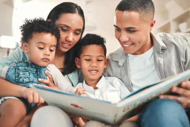 Photo of Shot of a young family reading a book together on the sofa at home