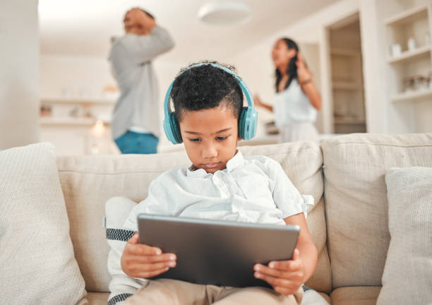 tiro de um menino usando um fone de ouvido e usando um tablet digital enquanto seus pais discutem ao fundo em casa - debt crisis audio - fotografias e filmes do acervo