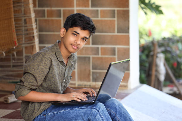 Indian boy using laptop while attending the online classes at home stock photo