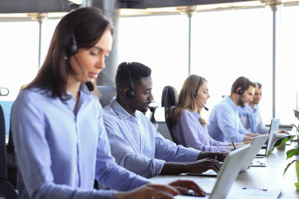istock Female customer support operator with headset and smiling, with collegues at background. 1368883464