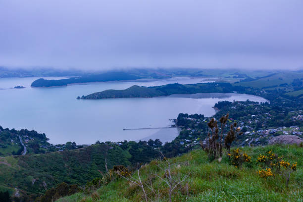This November 2021 dusk photo shows low clouds over Te Whakaraupō Lyttelton Harbour, Aotearoa New Zealand. The community of Governors Bay is in the centre. The community jetty, with its earthquake-collapsed section, is visible. This area is part of Horomaka Banks Peninsula in Ōtautahi Christchurch.