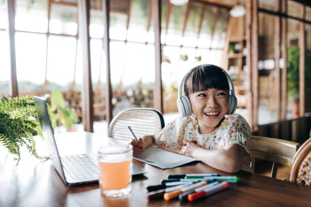 wesoła azjatka ze słuchawkami ucząca się z domu, uśmiechająca się radośnie. uczęszcza na zajęcia szkolne online z laptopem i pisze notatki w domu. e-learning, koncepcja edukacji domowej - digital tablet audio zdjęcia i obrazy z banku zdjęć
