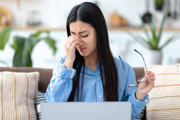istock Stressed tired from computer work asian woman feeling eye strain sitting at home on the couch, Headache, migraine 1368887633