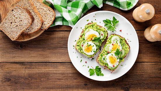 Healthy breakfast toast with avocado smash and boiled egg. Wood background. top view