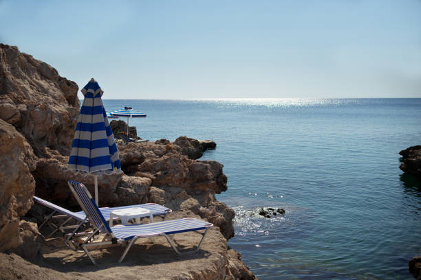 Close view of sunbeds and umbrellas on rocky seashore in Greece Rhodes Kalithea