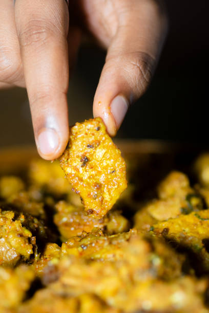 Human hand picking up cooked and spicy chicken piece for eating.