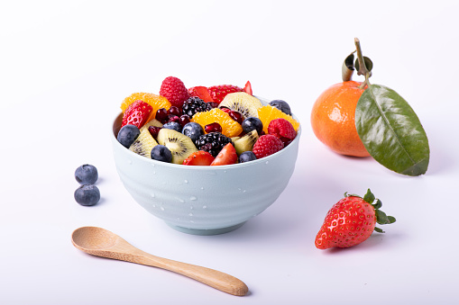 Fresh mixed fruit salad in a bowl with a wooden spoon in the foreground. White background