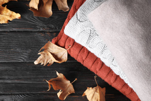 istock Stack of folded warm sweaters and dry leaves on black wooden table, top view 1368903291