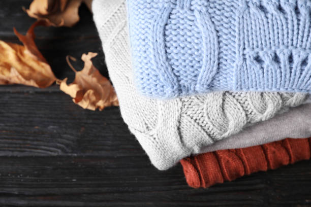 istock Stack of folded warm sweaters and dry leaves on black wooden table, above view 1368903436