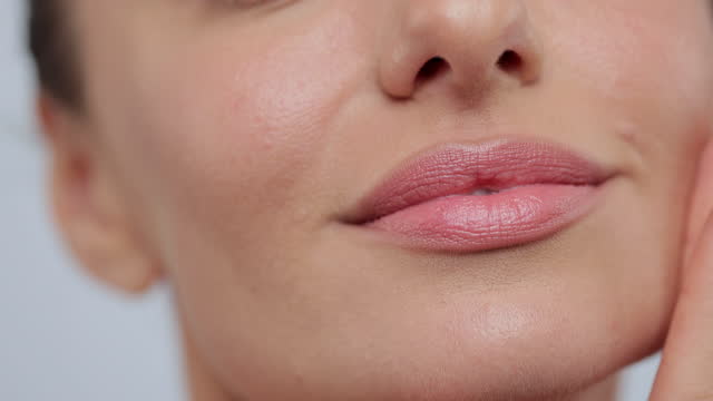 Close up feminine lips and chin applying anti aging cream on face skin. Women demonstrate moisturizing facial care touching cheek isolated on gray studio background. Skincare concept.
