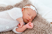Newborn baby in white knitted suit sleep in wooden basket.