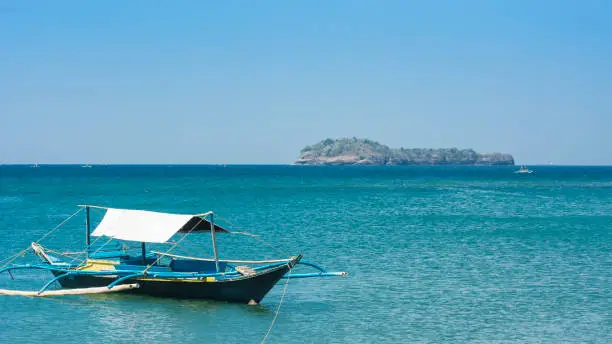 Photo of A small tourist outrigger boat is moored near Calayo Beach, while Loren island is visible in the background. A popular beach and island hopping area for local tourists. In Nasugbu, Philippines.