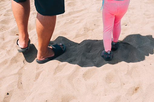 A man and his daughter walks through the sand on their way to the beach. Father and daugther bond. Summertime concept.