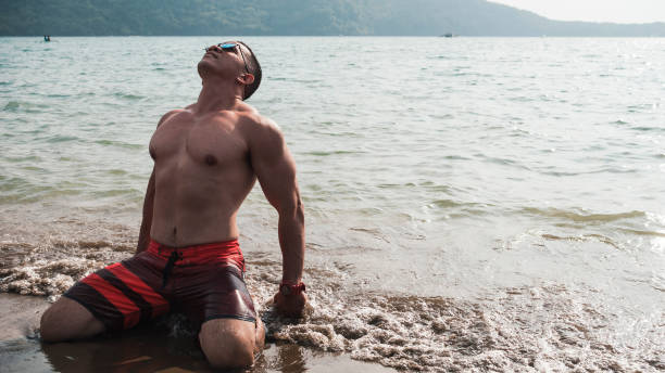 istock A fit and muscular man does some stretching while kneeling on the beach. Hands on ankles. 1368910649