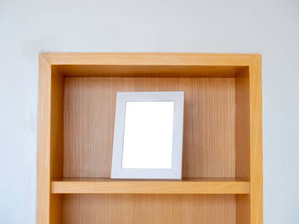 istock Mockup of a white square picture frame, vertical style. Blank white picture frame on the top shelf on the wood cupboard, minimal style. 1368910866