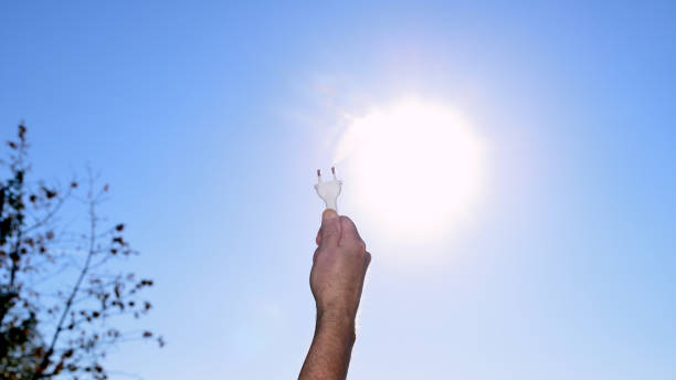 Sustainable energy supply. Because of climate change needs to instal solar panels or wind turbines increase to be \nenergetic self-sufficiency. Man holding arm in the air with a electrical plug in his hand pointing to the sun in autumn in the afternoon