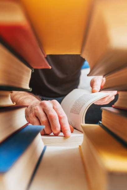 istock Through a stack of books a view of a reading man in a library - scientific 1368912949