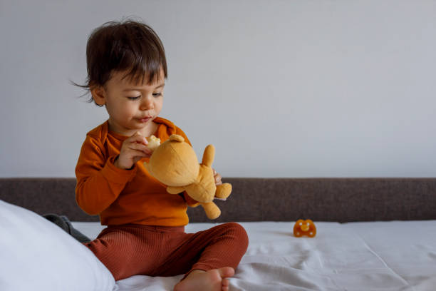 istock A small child with a banana in his hand feeds a toy while sitting on the bed. 1368913049