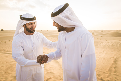 Arabian men with kandora walking in the desert - Portrait of two middle eastern adults with traditional arabic emirates dress