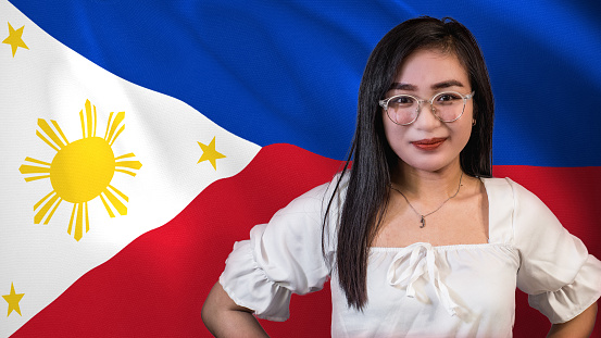 A proud and patriotic young Filipina woman, in front of a waving Philippine flag.